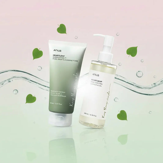 Deux produits de la marque Anua sont présentés côte à côte sur un fond dégradé rose et vert pastel, entourés de feuilles de cœur et de gouttelettes d’eau. À gauche se trouve un tube vert de mousse nettoyante, et à droite un flacon pompe transparent d’huile démaquillante, tous deux avec la mention “Keep things simple” sur l’emballage.