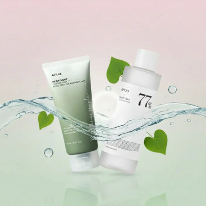 Deux produits cosmétiques de la marque Anua sont présentés sur l’image : à gauche, une mousse nettoyante visage et à droite, un toner Heartleaf 77%. Les deux produits sont entourés d’une éclaboussure d’eau transparente et de feuilles vertes en forme de cœur, sur un fond dégradé pastel allant du rose au vert, évoquant la fraîcheur et la pureté.