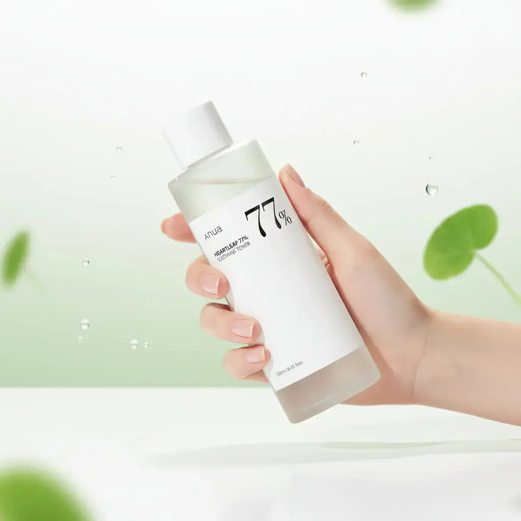 Une main tient une bouteille de toner Anua Heartleaf 77% devant un fond vert pâle, avec des feuilles de cœur en arrière-plan et des gouttelettes d’eau dispersées autour, créant une atmosphère fraîche et naturelle.